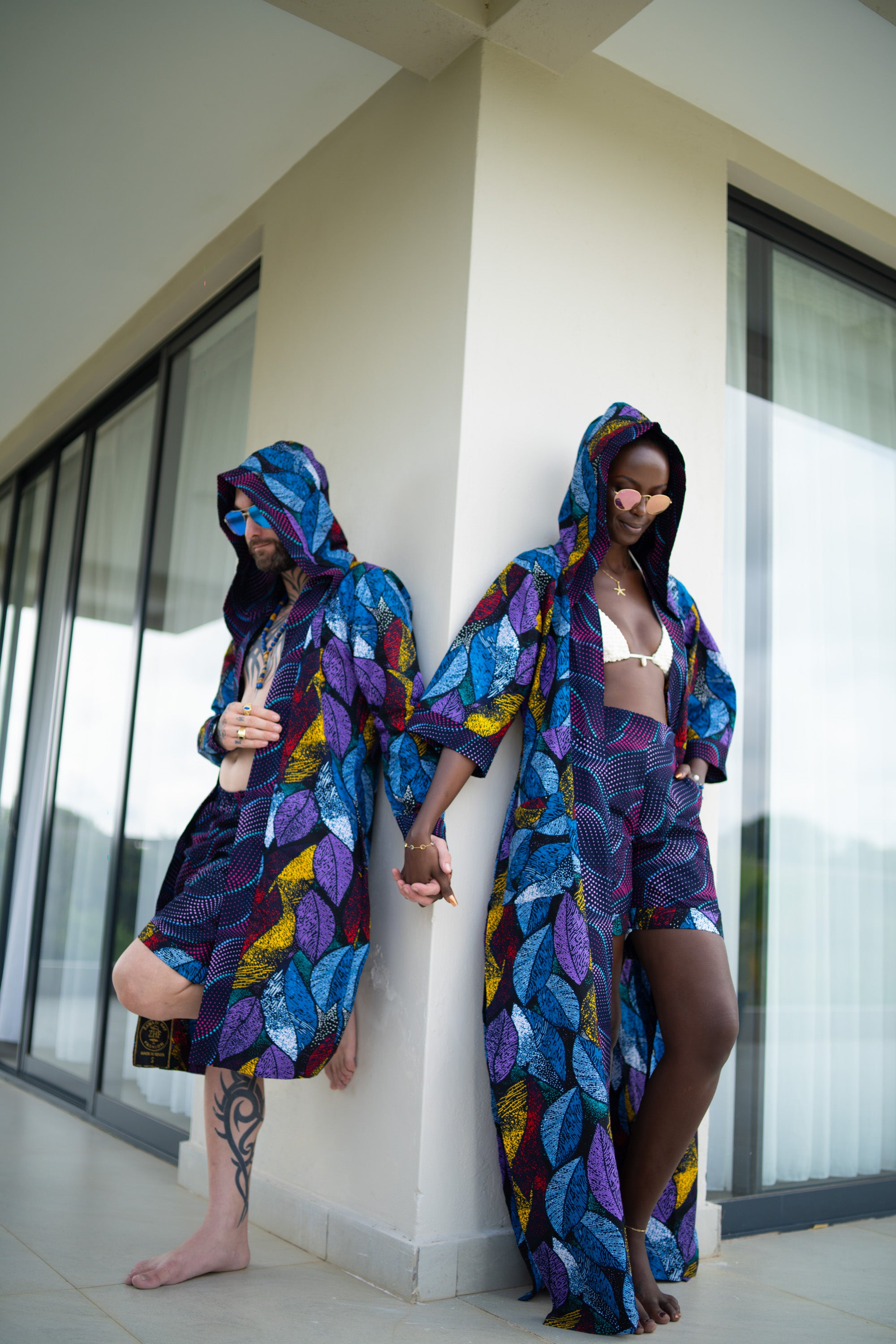 A interracial couple wearing colorful wax cotton hooded outfits standing against each other