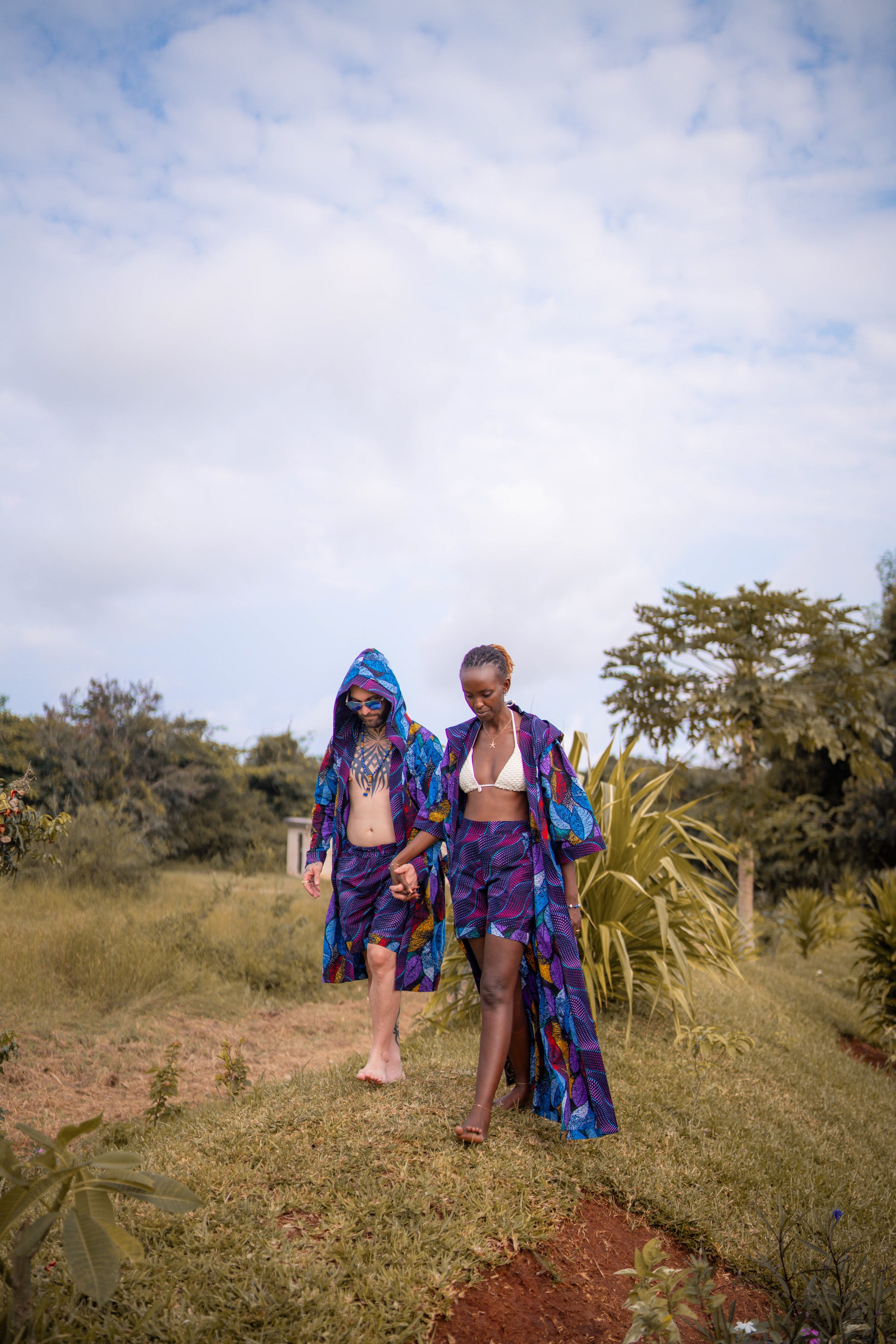 An interracial couple, holding hands, walking outdoors in a natural setting with colorful modern african clothing.