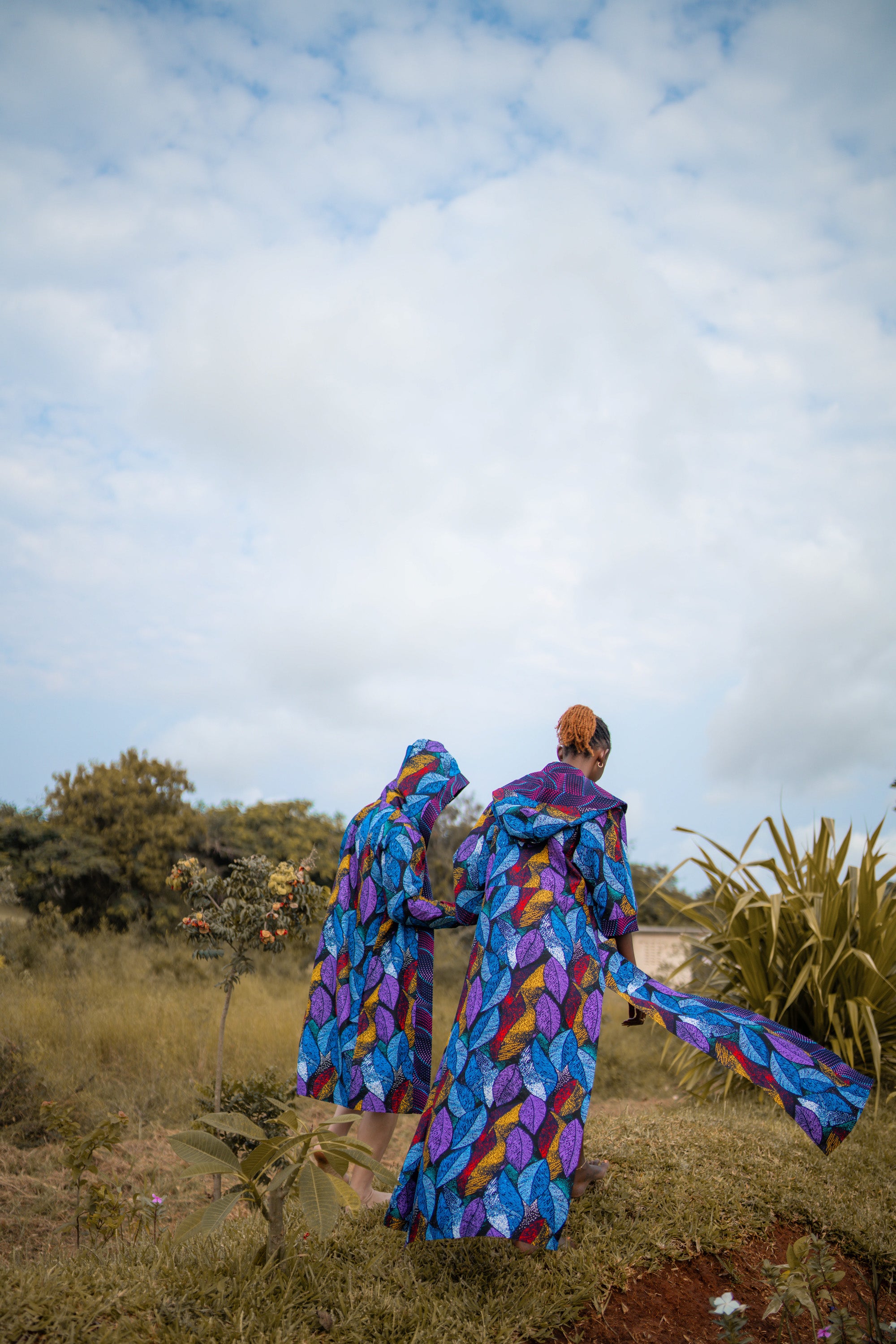 A couple dresed in colorful,african, patterned kimono walking through a field with a blue sky.