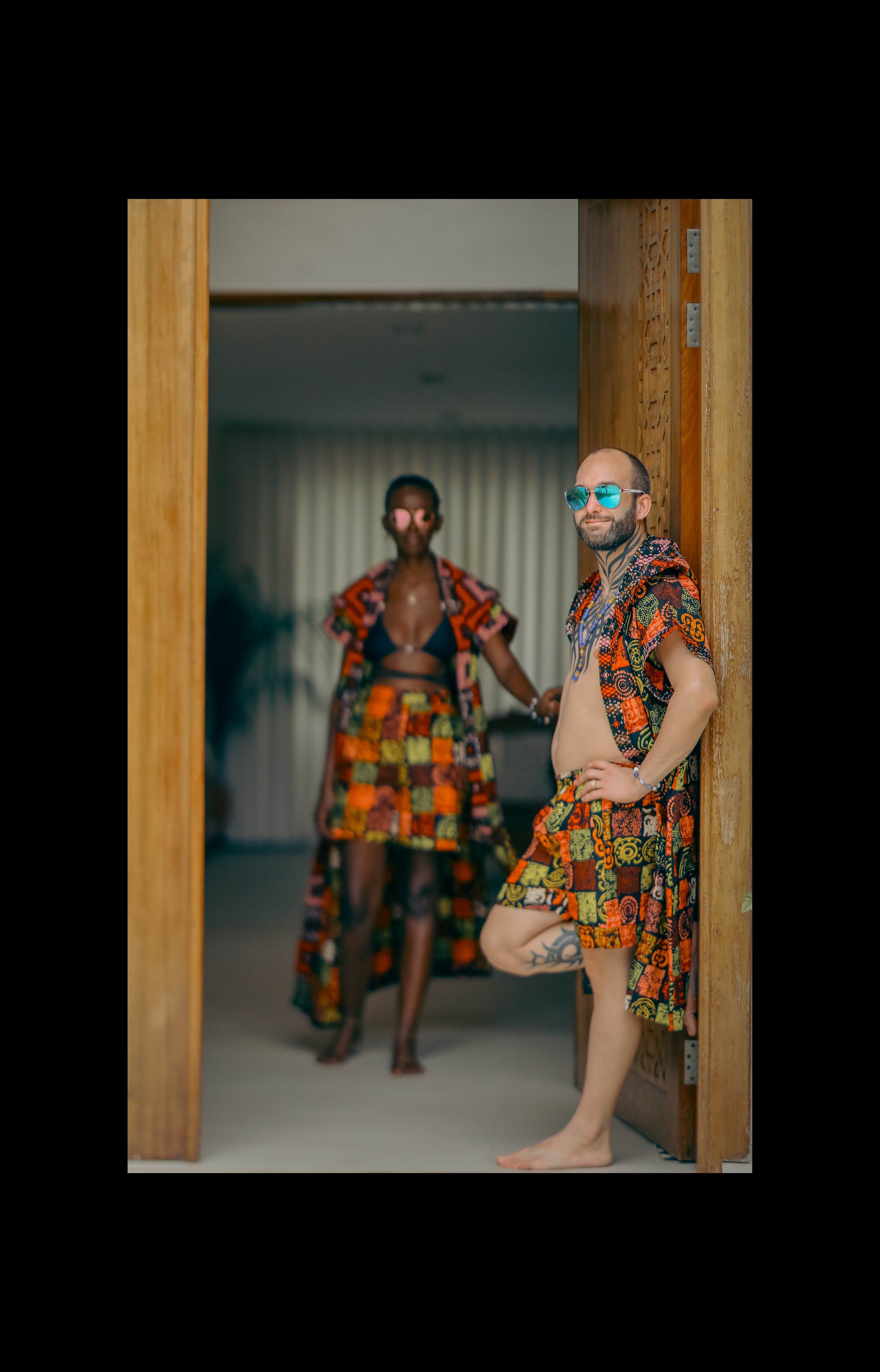 A couple styling Electric Safari African cover-up and shorts set in safari-inspired print – Zawadi Hat  standing in a doorway.