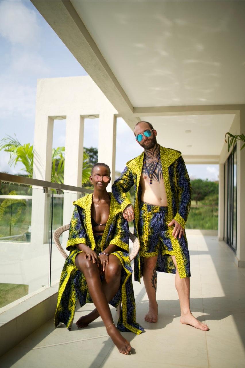 A couple styling Electric Safari African cover-up and shorts set in safari-inspired print – Zawadi Hat on a balcony with a scenic background.