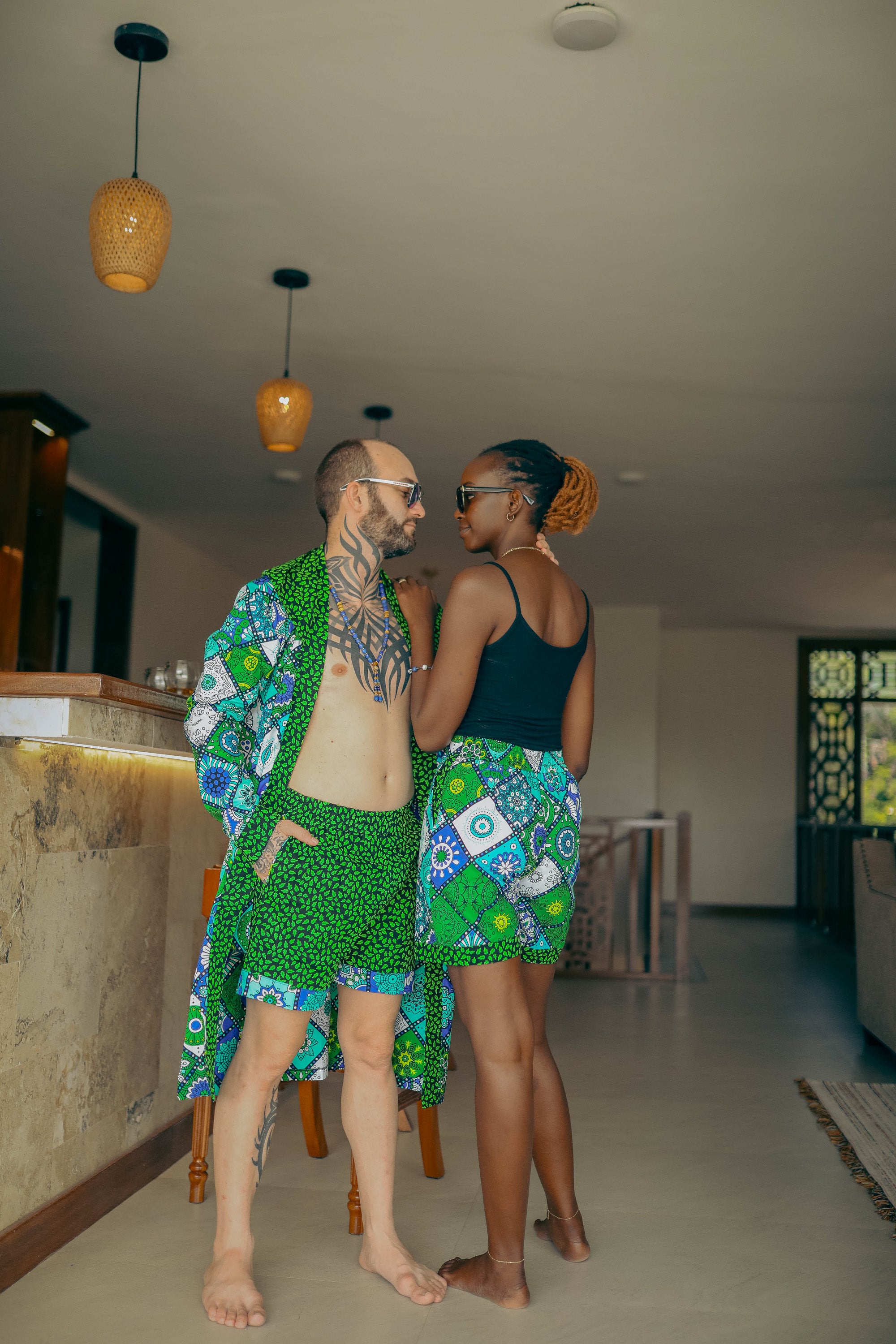 A couple in matching green and blue patterned outfits standing close together showcasing outfit from zawadi hat fashion