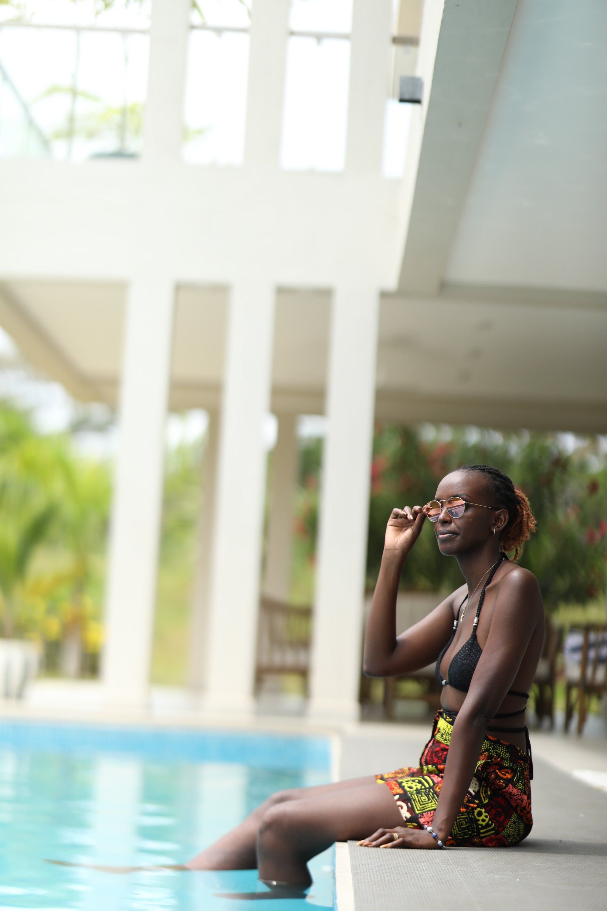Woman styling Electric Safari African short safari-inspired print – Zawadi Hat sitting by a pool with blurred background