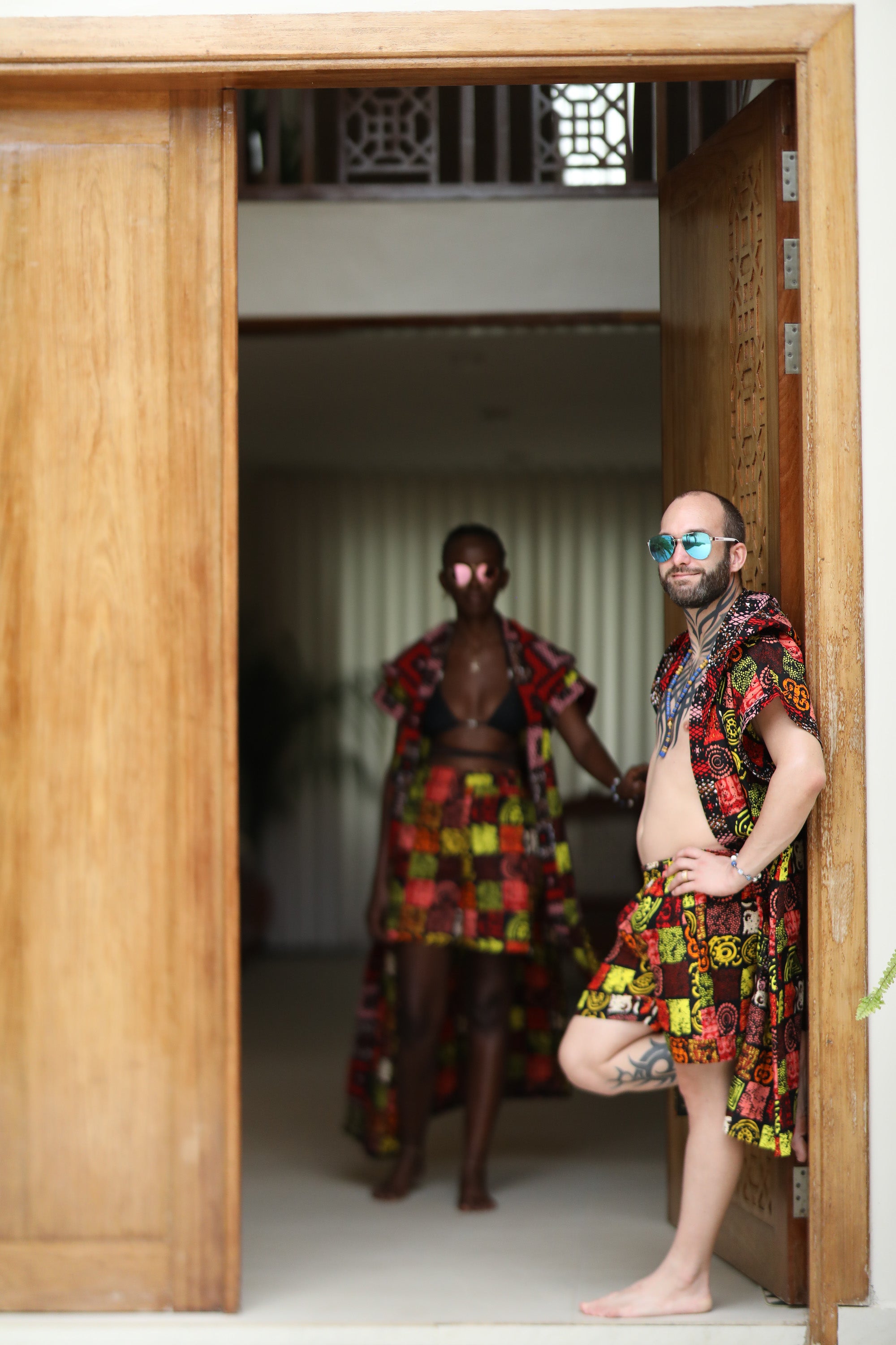 A couple styling Electric Safari African cover-up and shorts set in safari-inspired print – Zawadi Hat standing in a doorway.
